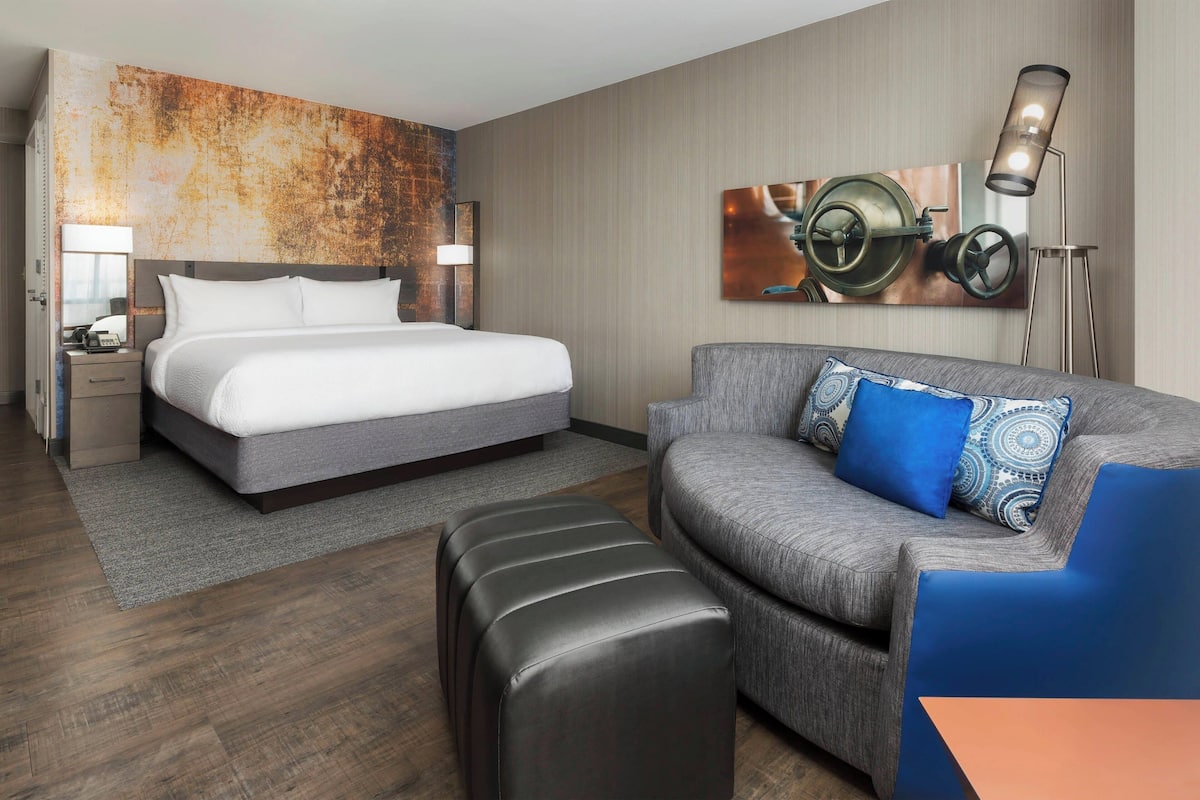 A modern hotel room with a large bed, a grey sofa, and a coffee table.
