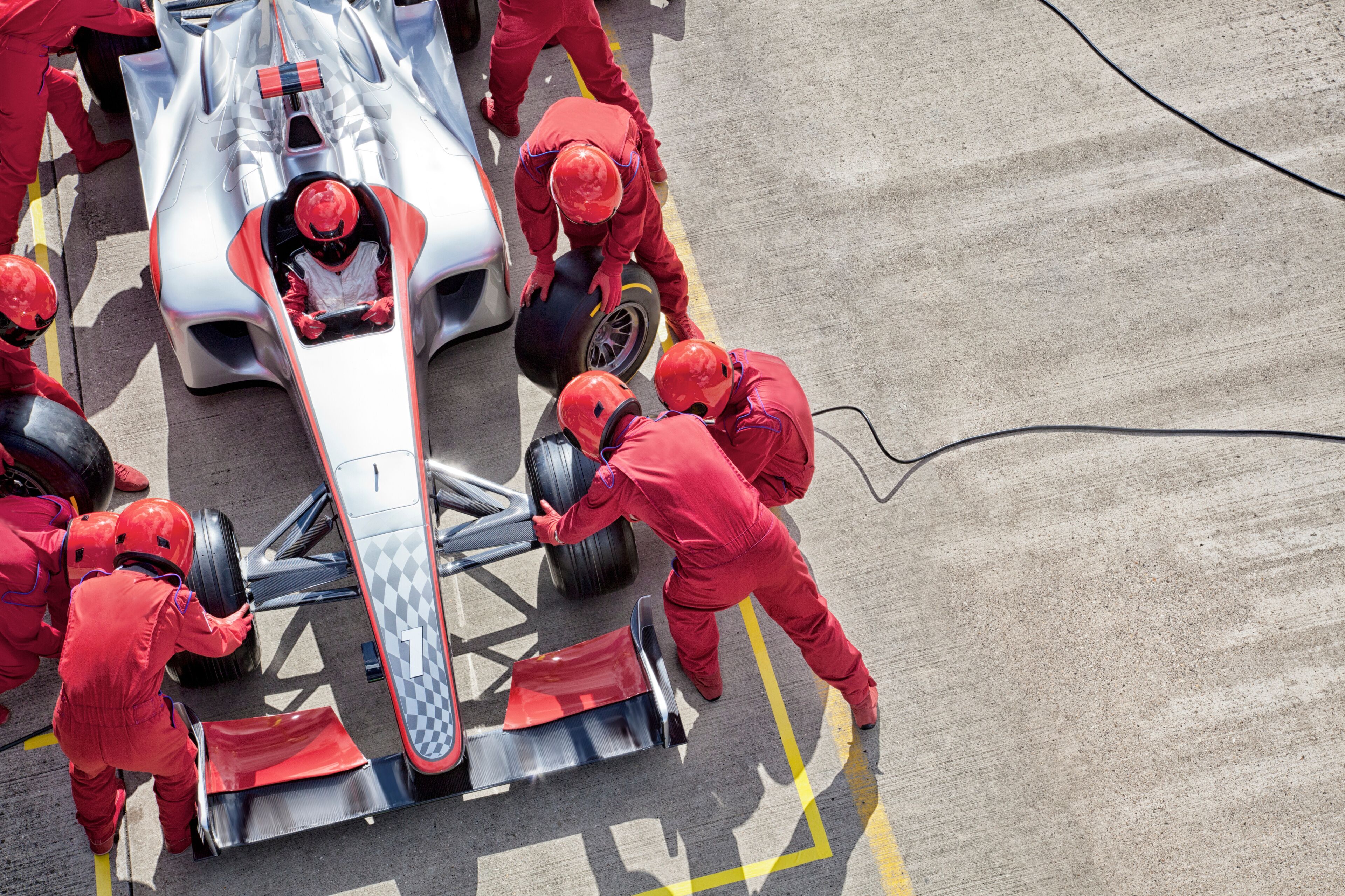 Une voiture de course performante, sur laquelle plusieurs mécaniciens vêtus d’uniformes rouges sont en train de travailler.
