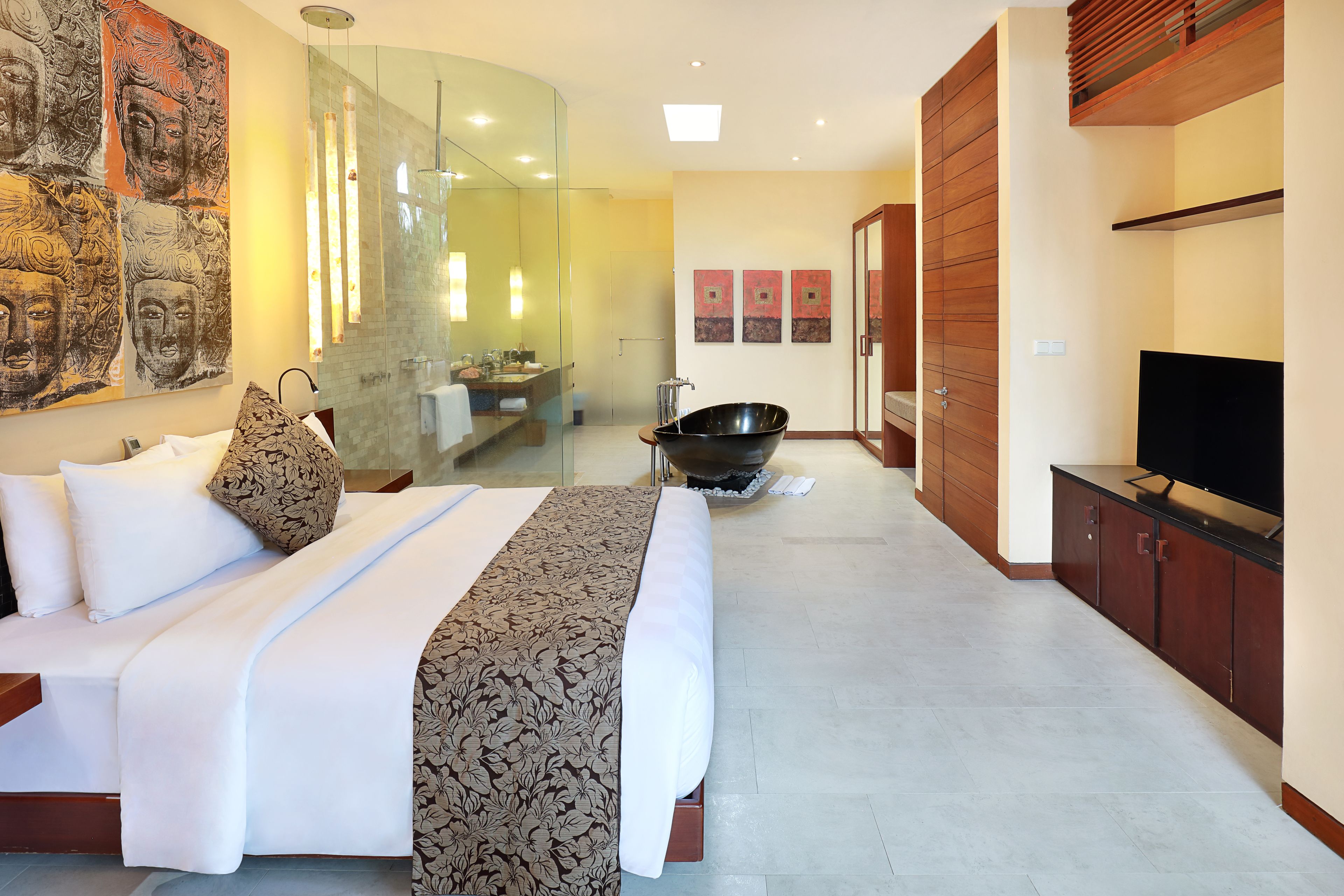 A modern hotel room with a large bed, a glass-enclosed shower, a black bathtub, a television, and artwork on the walls.