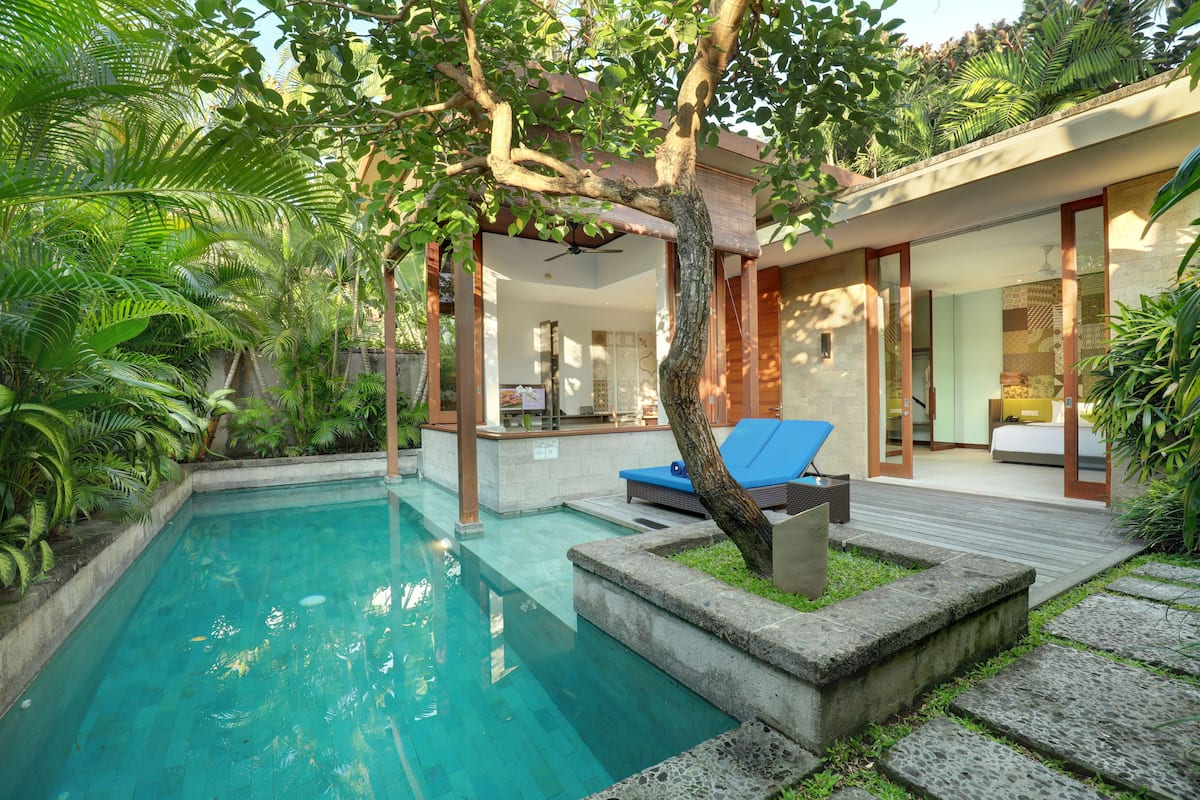 Piscina cercada por vegetação exuberante, um deck de madeira e uma casa moderna com amplas janelas.