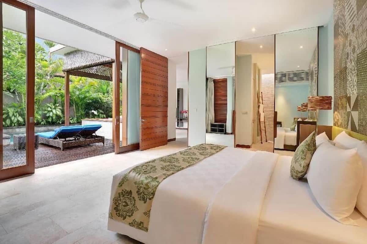Quarto de hotel moderno com uma cama grande, porta de vidro que dá para uma área de piscina e vista para vegetação exuberante.