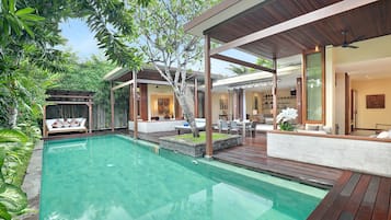 Uma área de piscina moderna ao ar livre, com deck de madeira, espaço de estar com sofá e cadeiras, e um alpendre coberto.