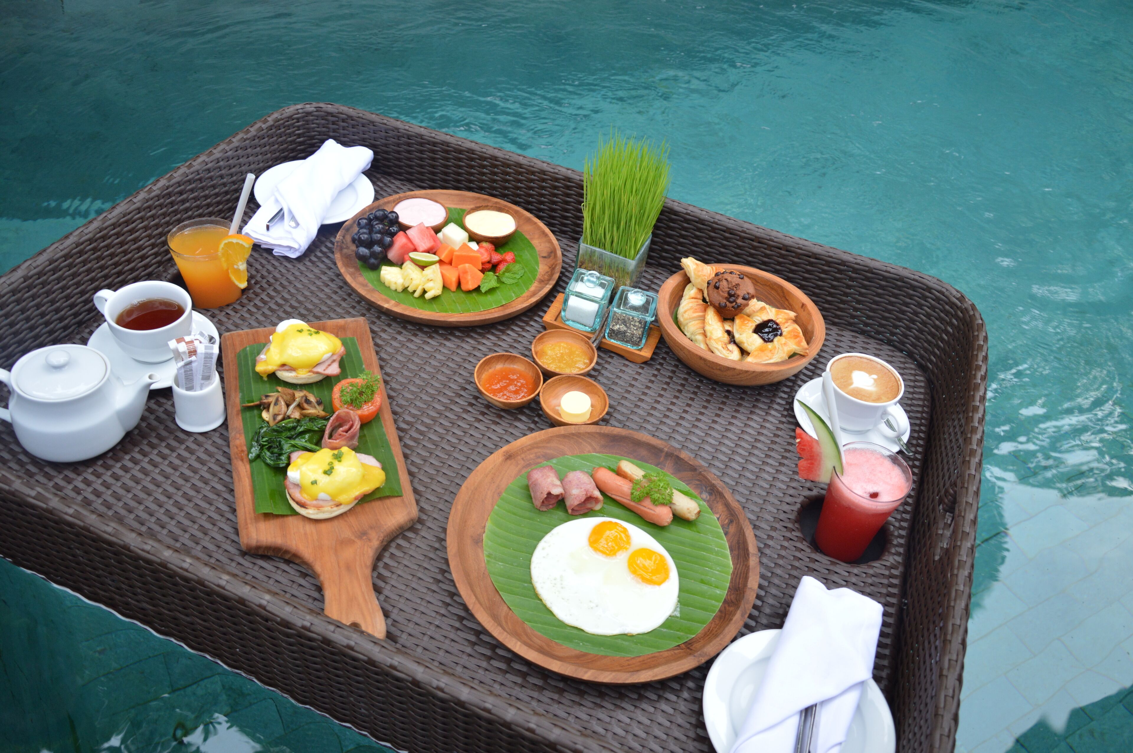 A breakfast tray with various foods and drinks by a pool.