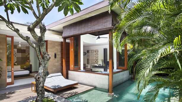 A modern outdoor pool area with a wooden deck, a lounge chair, and a small table. - The Elysian Boutique Villa Hotel (Seminyak)