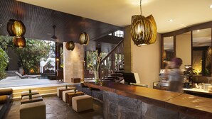 A modern lobby with a stone reception desk, seating area, and a staircase leading to a pool area. - The Elysian Boutique Villa Hotel (Seminyak)
