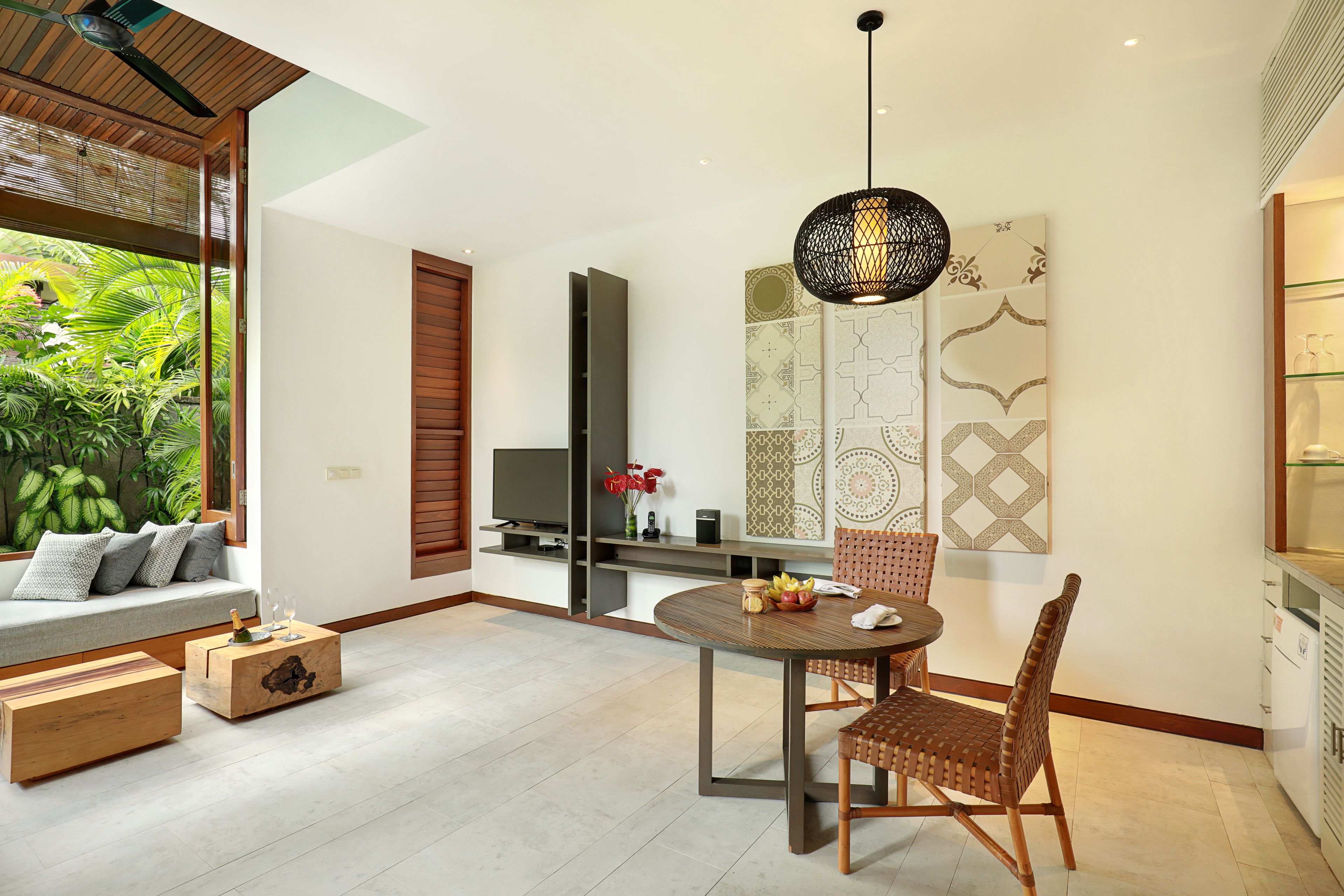 A modern living room with a dining area, a TV, and a view of greenery.