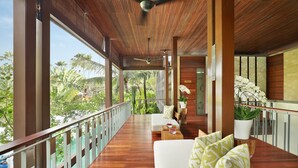 A wooden deck with a railing, a white sofa with patterned cushions, and a potted plant. - The Elysian Boutique Villa Hotel (Seminyak)