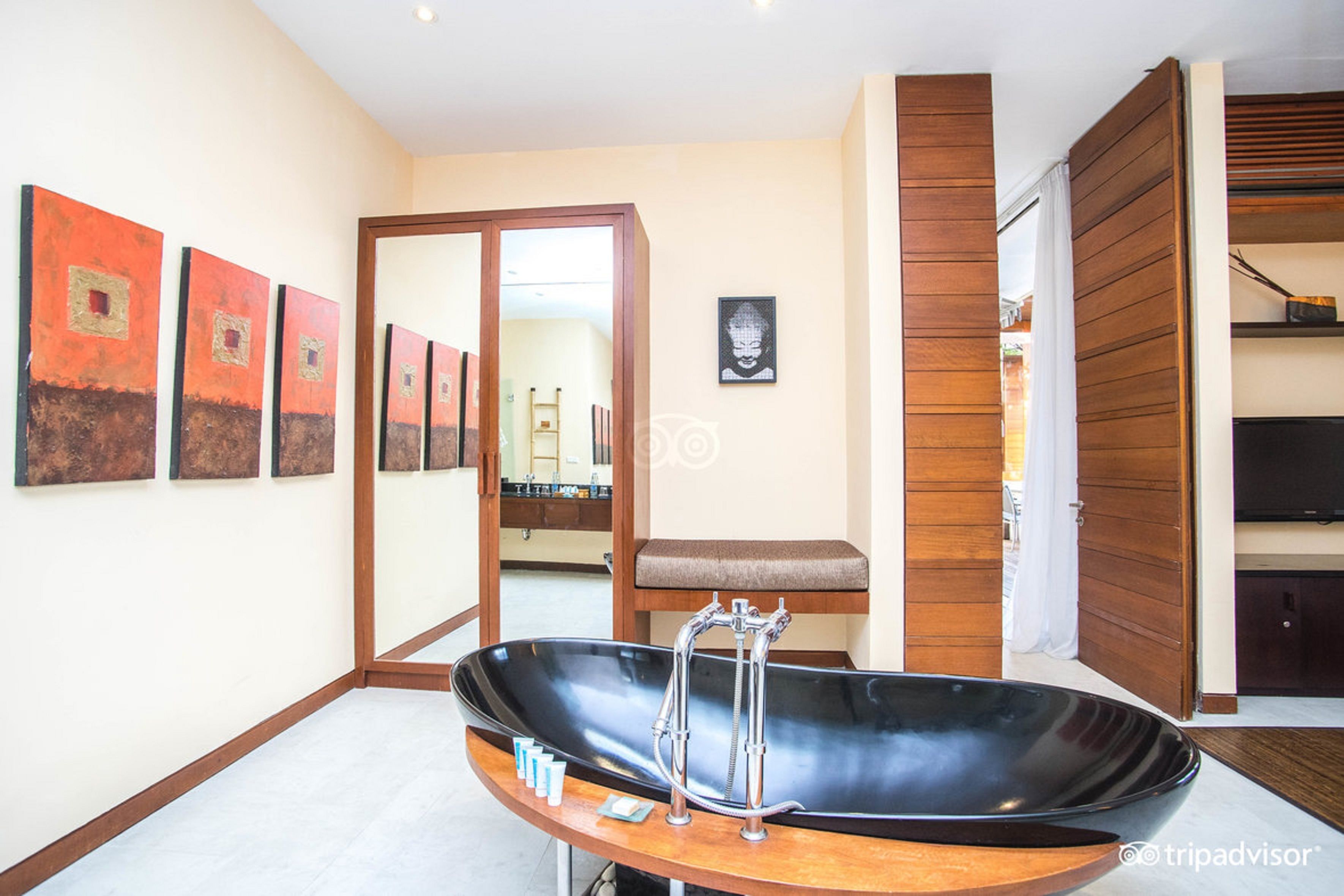 Une salle de bain moderne avec une grande baignoire noire, un lambris en bois et un miroir qui reflète la pièce.
