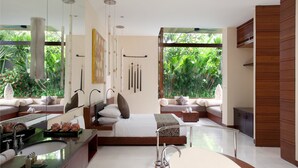 A modern bedroom with a large bed, a glass-enclosed bathroom, and a view of lush greenery. - The Elysian Boutique Villa Hotel (Seminyak)