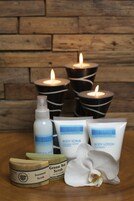Ambiente de spa com velas, produtos de cuidados corporais e uma orquídea.