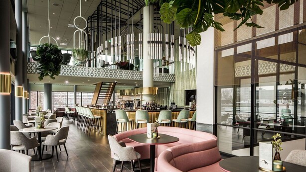 A modern interior with a bar area, seating arrangements, and hanging plants. - Van der Valk Hotel Haarlem (Haarlem)
