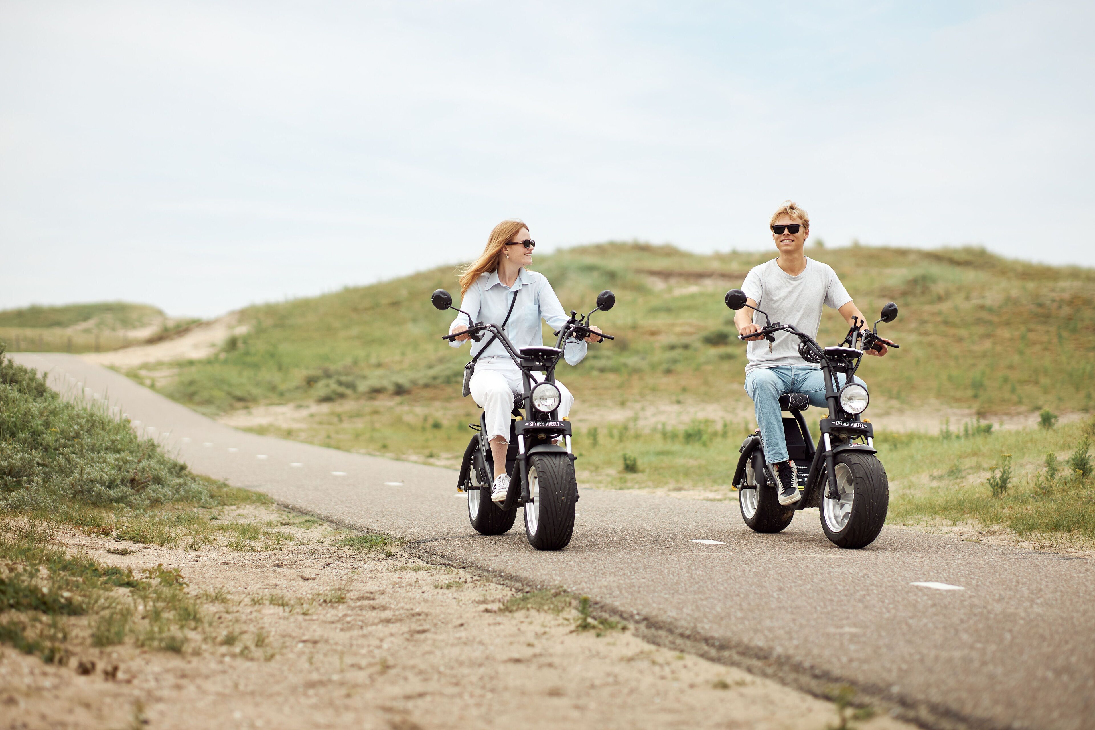 Dos personas paseando en scooters eléctricos por un camino pavimentado en un entorno natural.