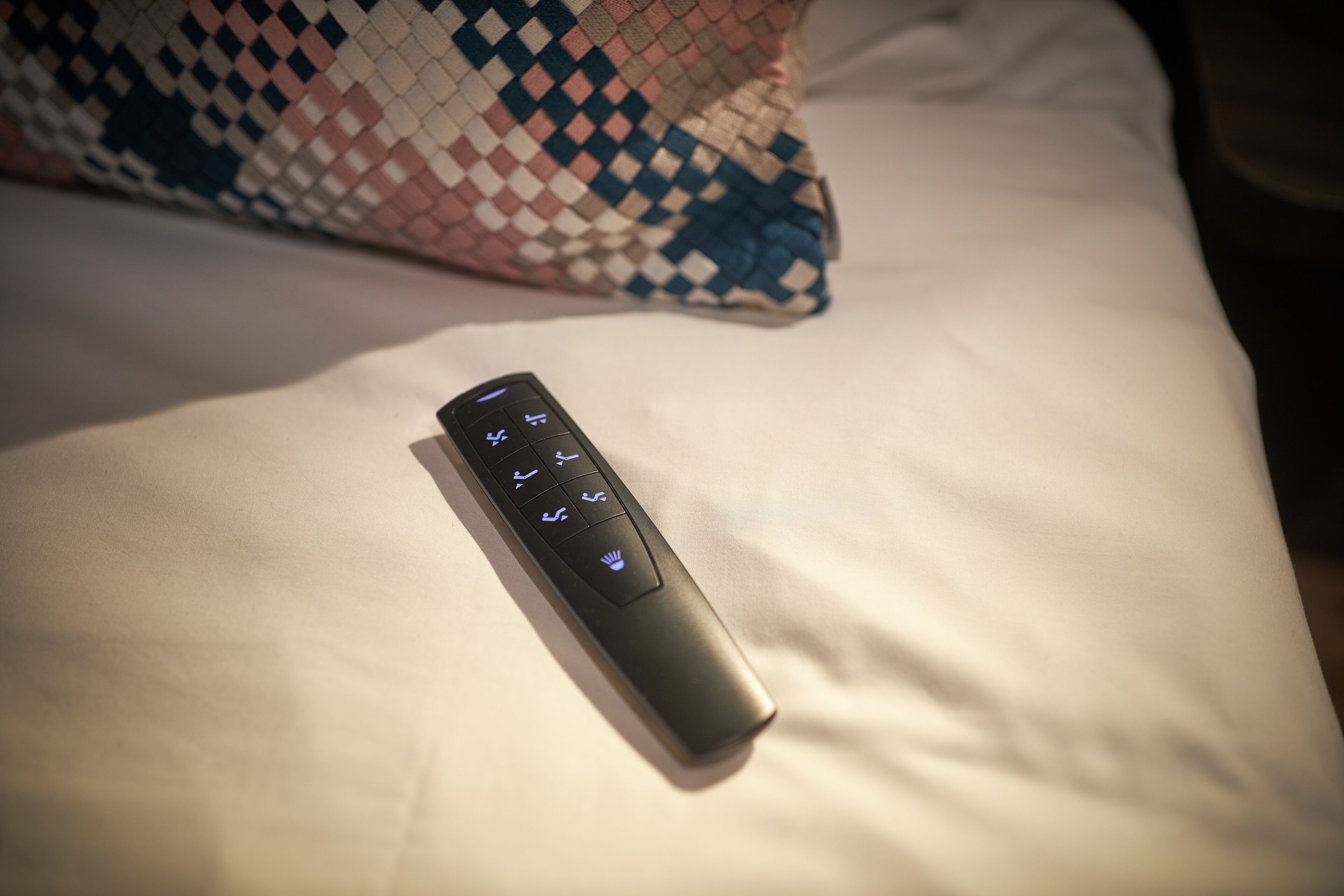 Un control remoto sobre una cama con un cojín estampado.
