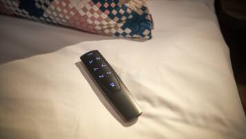 Un control remoto sobre una cama con un cojín estampado.