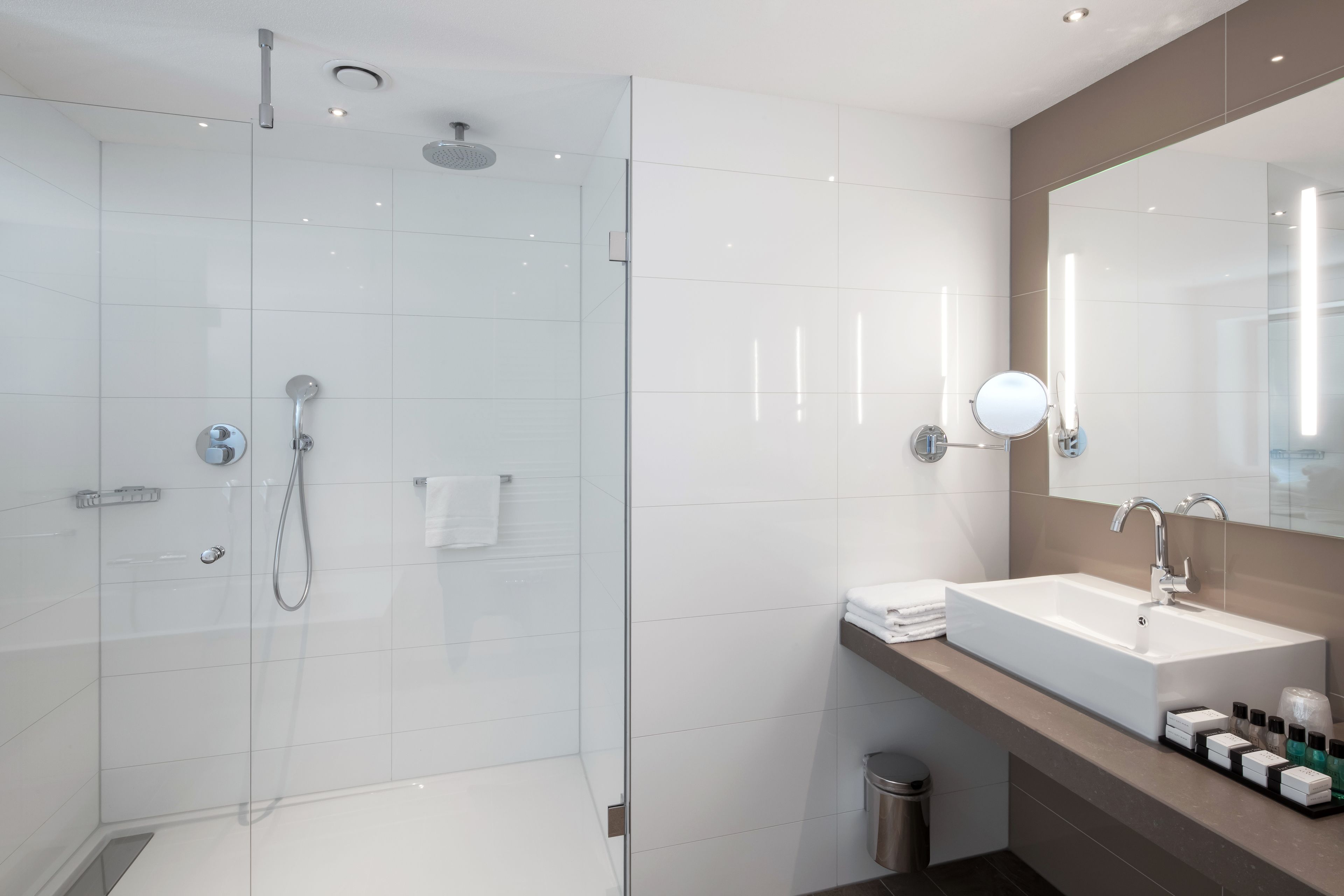 Een moderne badkamer met een douche in een glazen cabine, een grote spiegel en een wastafel met toiletartikelen.
