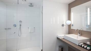 Een moderne badkamer met een douche in een glazen cabine, een grote spiegel en een wastafel met toiletartikelen.