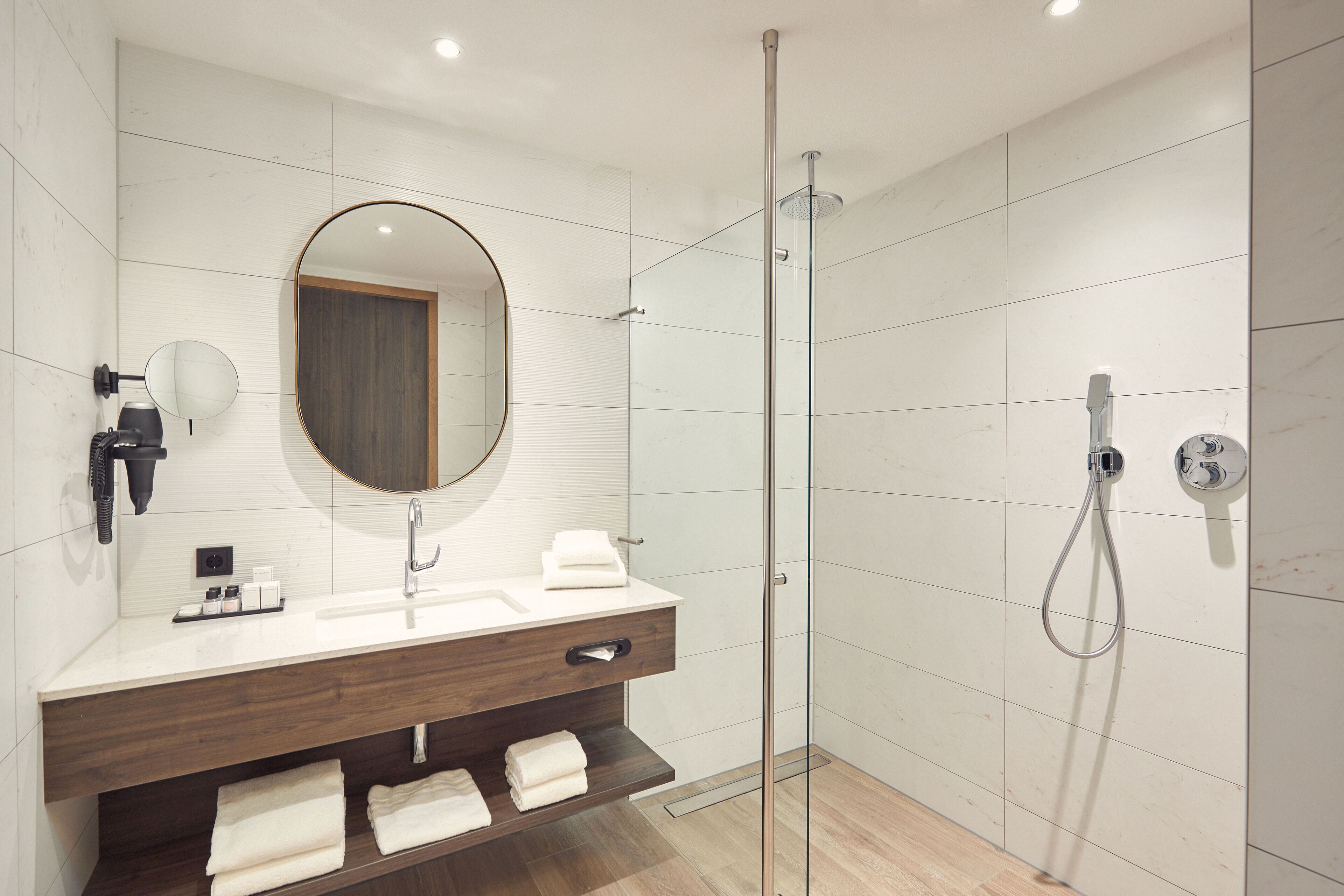 A modern bathroom with a glass-enclosed shower, a wooden vanity with a mirror, and a white sink.