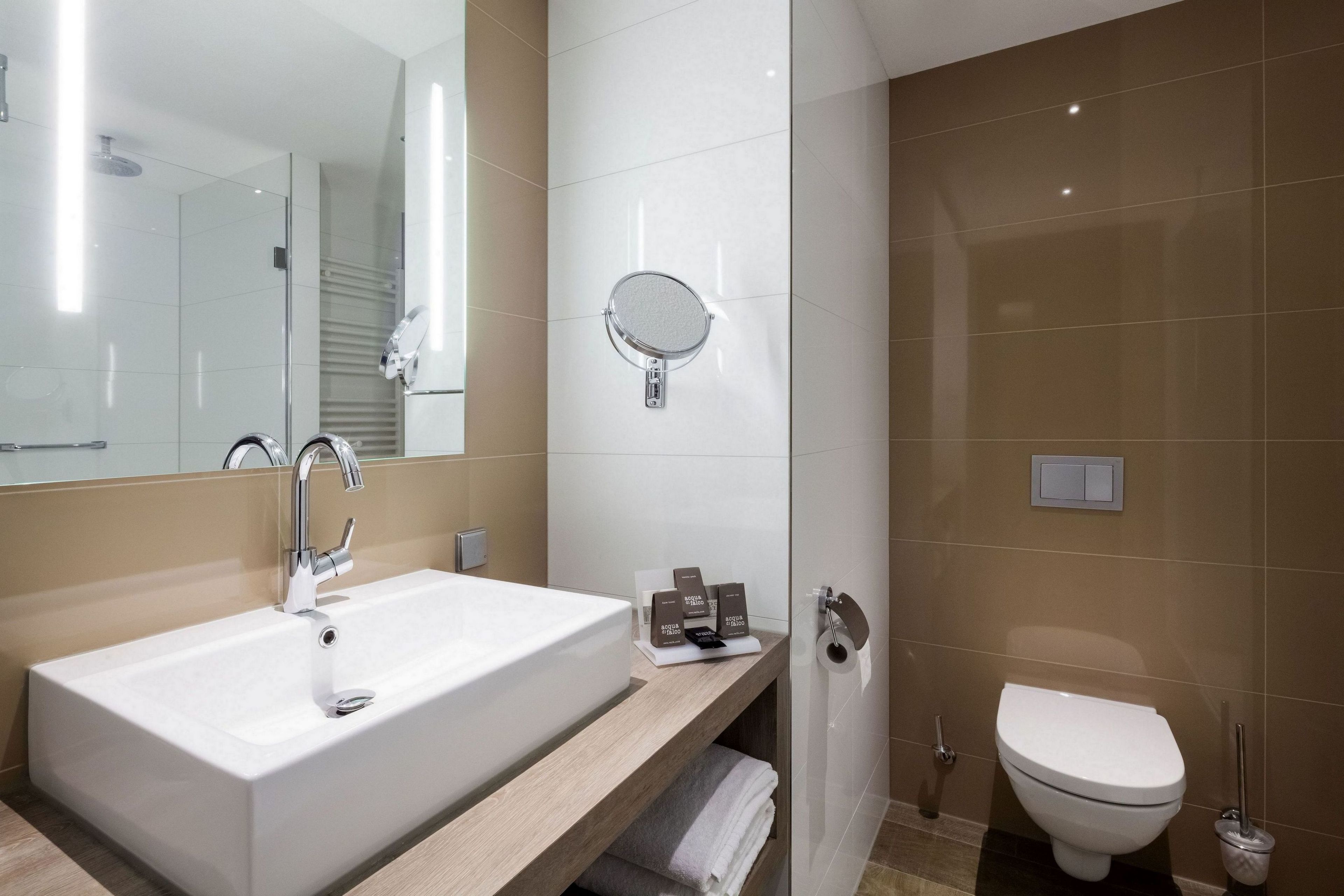 A modern bathroom with a large sink, a mirror, a toilet, and a towel rack.