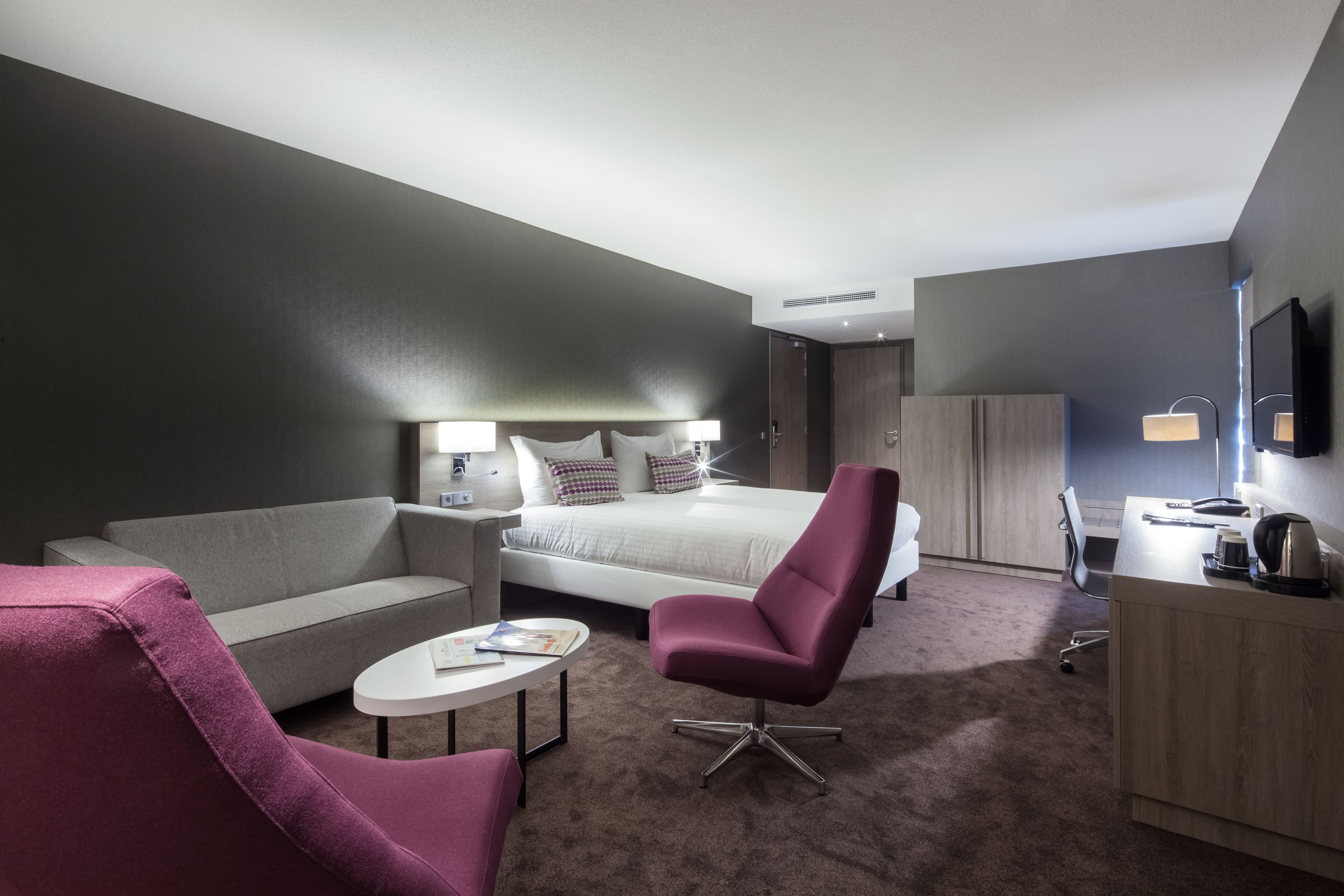 Una habitación de hotel moderna con una cama, un escritorio, una silla, un sofá y una mesita.