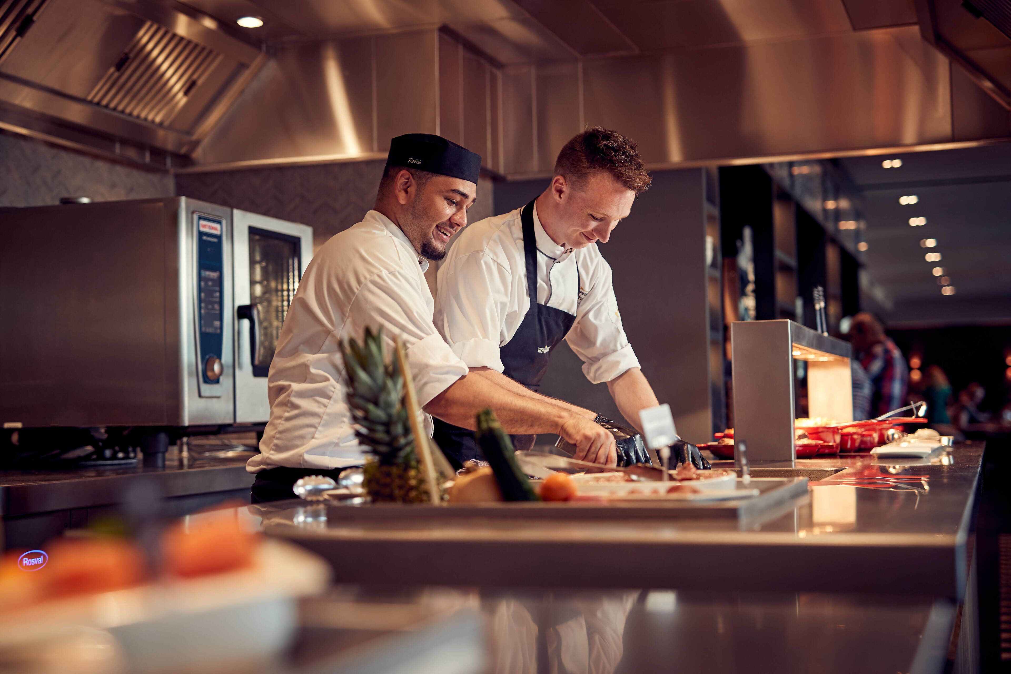 Deux chefs dans une cuisine moderne, dotée d’appareils électroménagers en acier inoxydable et d’un plan de travail poli.