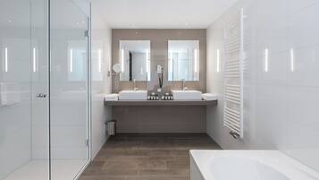 A modern bathroom with a glass shower enclosure, two sinks, a large bathtub, and a towel rack.