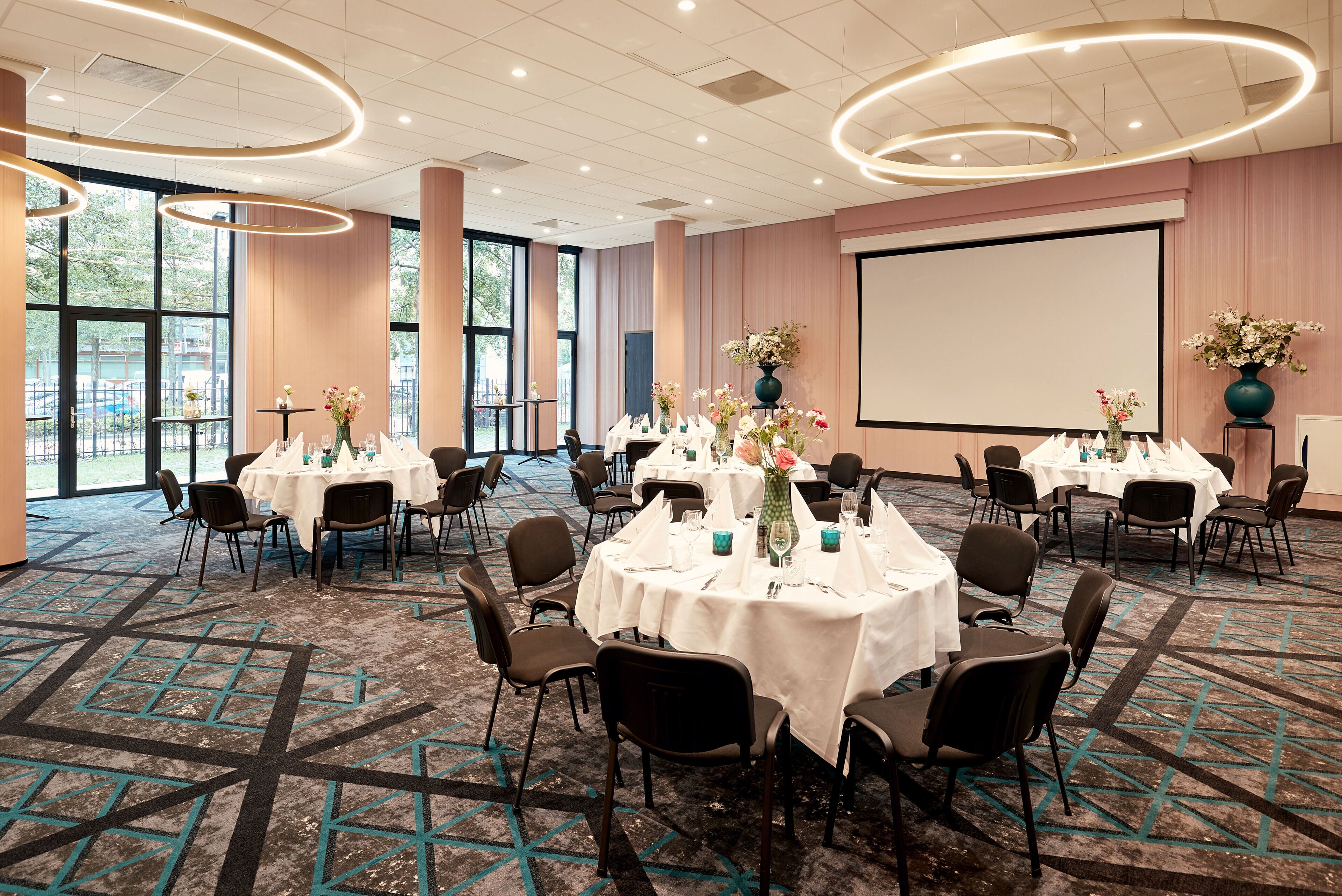 A conference room with multiple tables, chairs, and a large screen.
