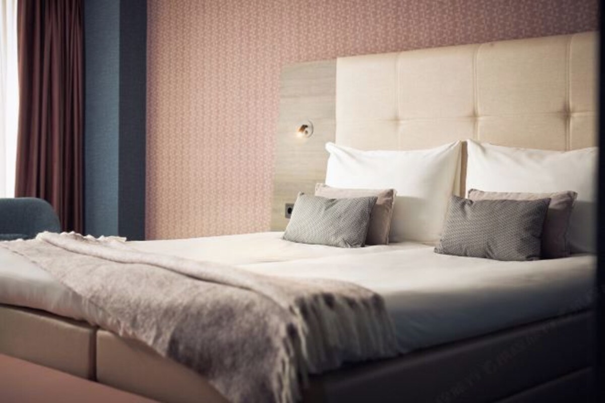A neatly made bed with a beige headboard, two pillows, and a blanket.