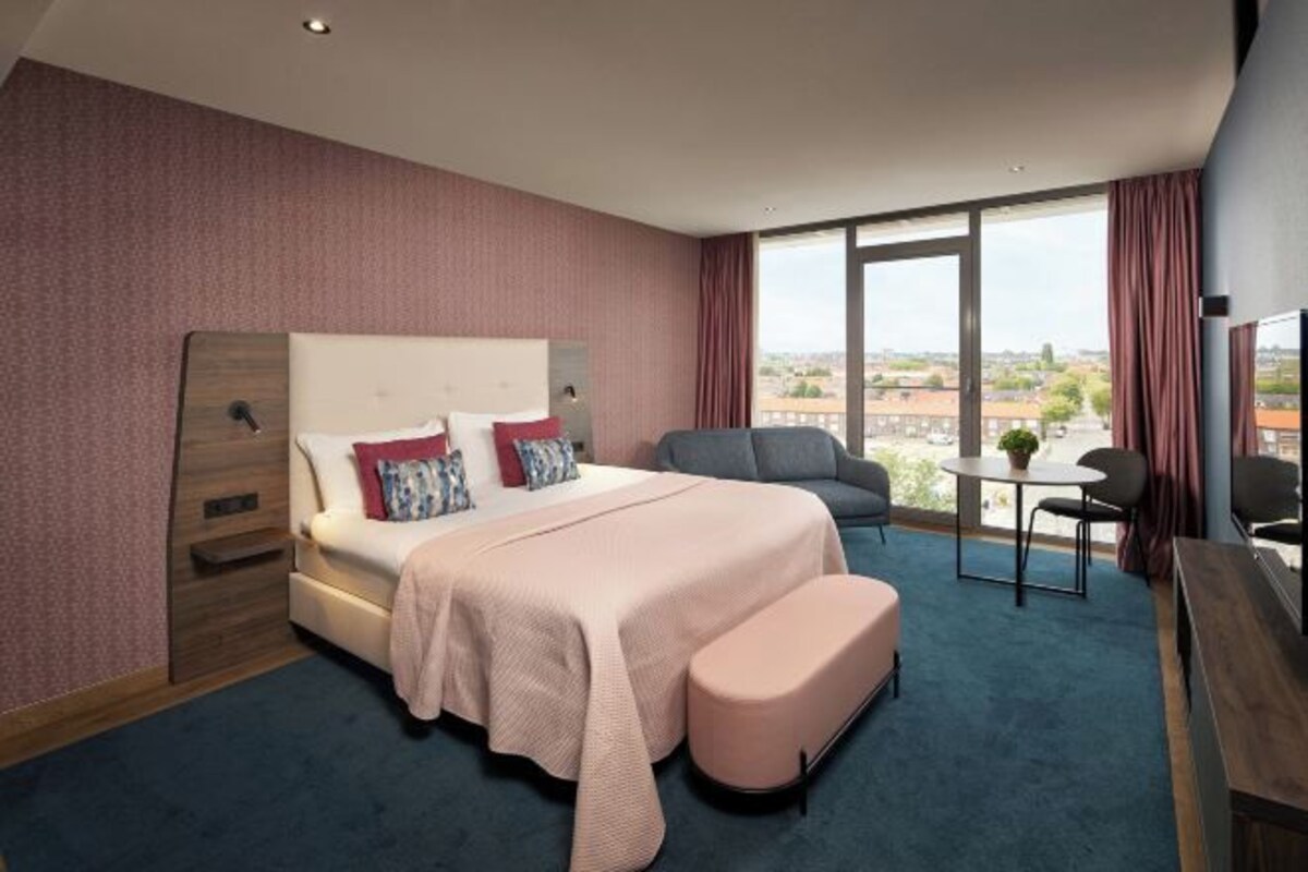 A hotel room with a large bed, a desk, a chair, and a view of the city.