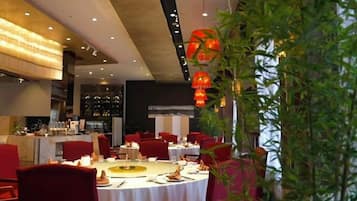 Un restaurant avec des tables rondes, des chaises rouges et un coin bar.