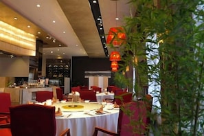 A restaurant with round tables, red chairs, and a bar area.