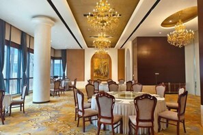 A conference room with round tables and chairs, chandeliers, and a large painting on the wall.