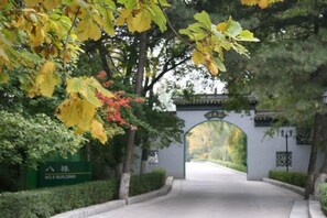 A pathway leading to a building entrance with a traditional archway, surrounded by trees and greenery.