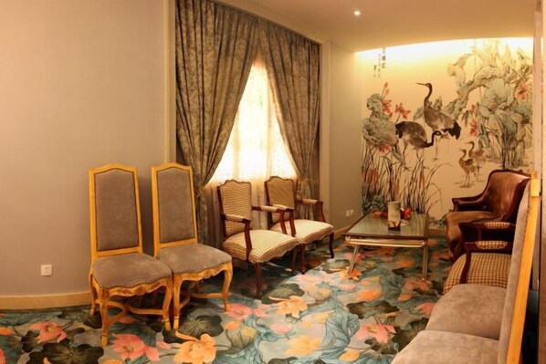 A room with a floral carpet, a large window with curtains, and a wall with a bird painting.