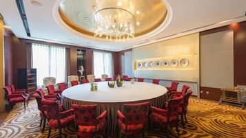 A conference room with a round table, red upholstered chairs, a chandelier, and a patterned carpet.