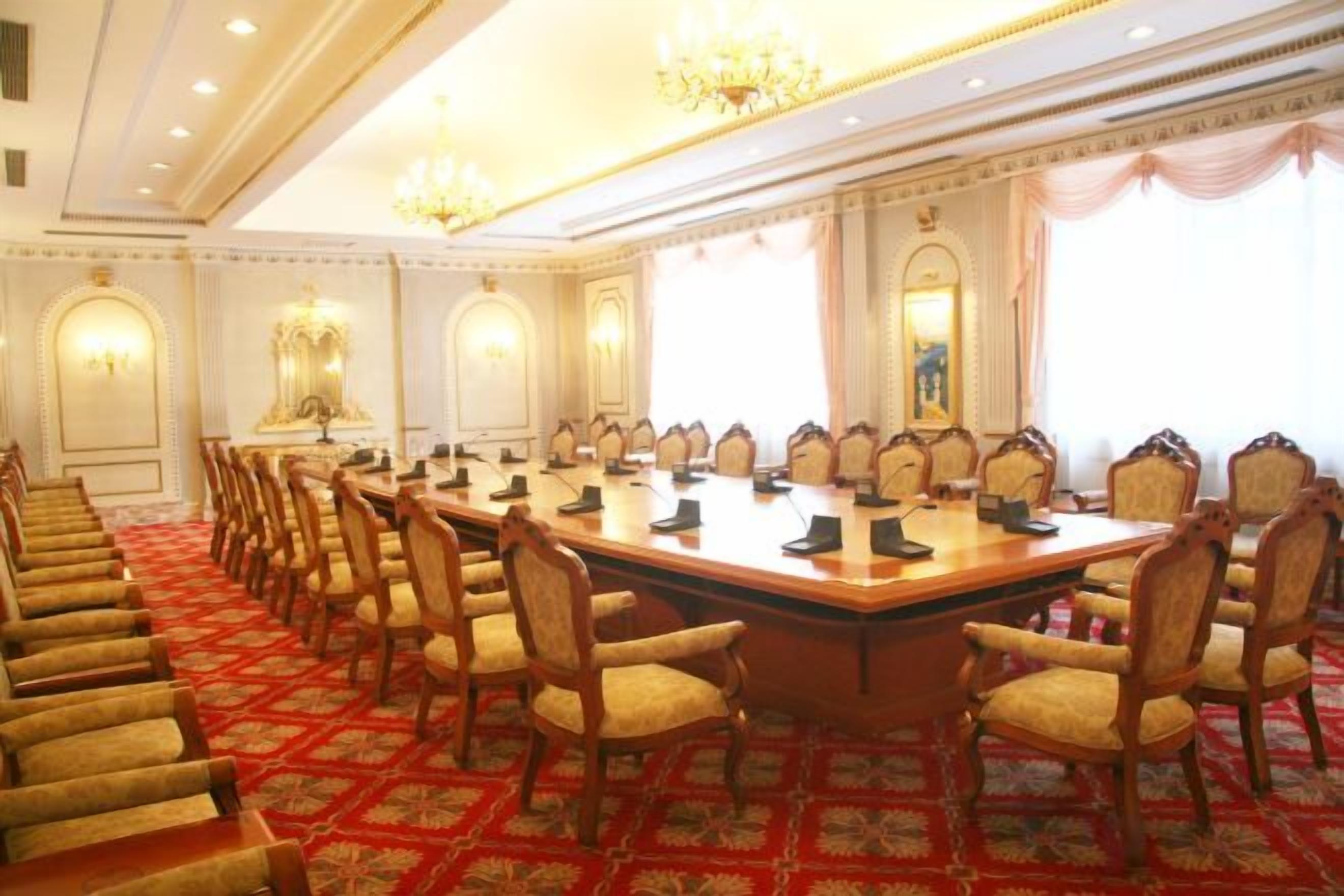 Een vergaderzaal met een lange tafel, meerdere stoelen en een vloerbedekking.