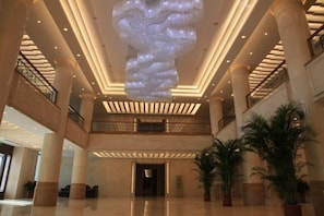 A spacious lobby with high ceilings, large columns, and a modern chandelier.
