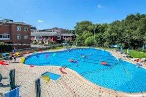 Una piscina con múltiples carriles, rodeada por una solana con baldosas y follaje.
