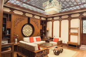 Een kamer in traditionele stijl met een houten plafond, een rond decoratief wandobject en een bank met kussens.