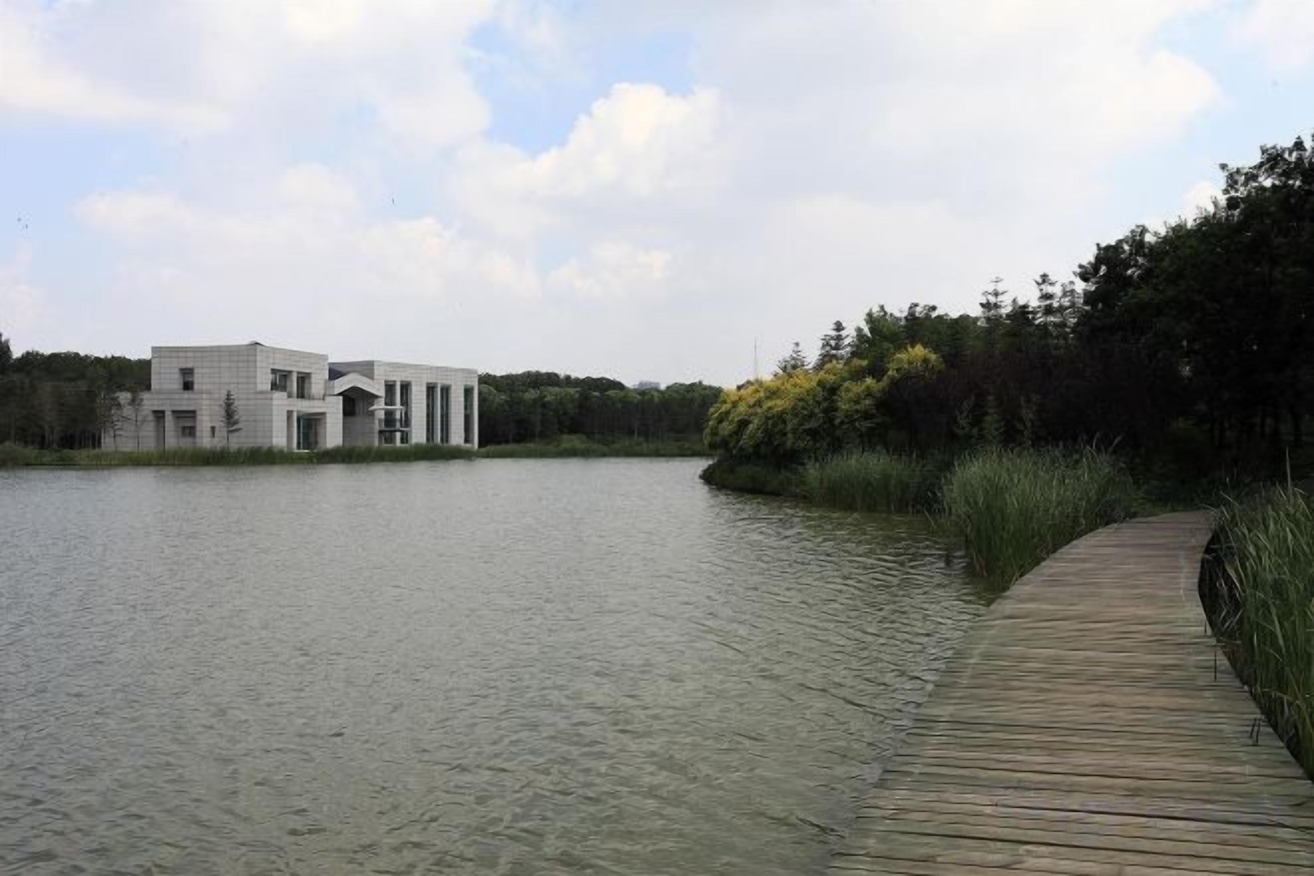 A modern building by a calm lake with a wooden dock leading to it.
