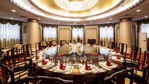 A round table set for a formal dinner with chairs around it, a chandelier above, and curtains on the windows. - Hongyi Hotel Wuhan University (Wuhan)