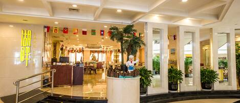Un hall de hotel con mostrador de recepción, escalera y plantas en macetas.