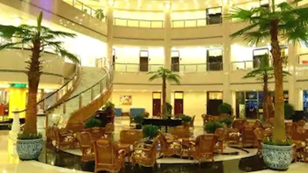 A multi-level atrium with a central staircase, palm trees, and seating areas. - Hongyi Hotel Wuhan University (Wuhan)