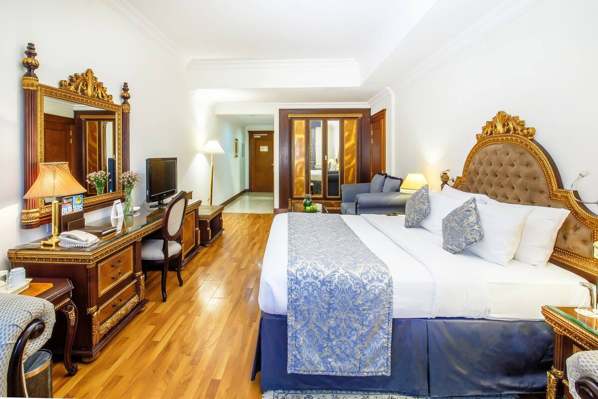 A hotel room with a large bed, a desk with a telephone, a chair, a television, and a mirror.