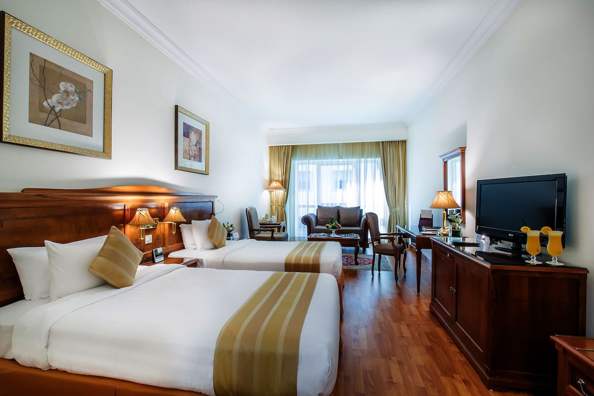 A hotel room with two beds, a TV, a desk, and a seating area with a sofa and chairs.