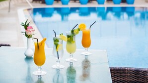 Un bar au bord de la piscine, avec trois cocktails et un vase de fleurs.