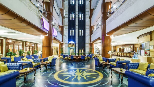 Un hall d’entrée spacieux avec des canapés bleus, un motif solaire central sur le sol et un comptoir d’accueil.