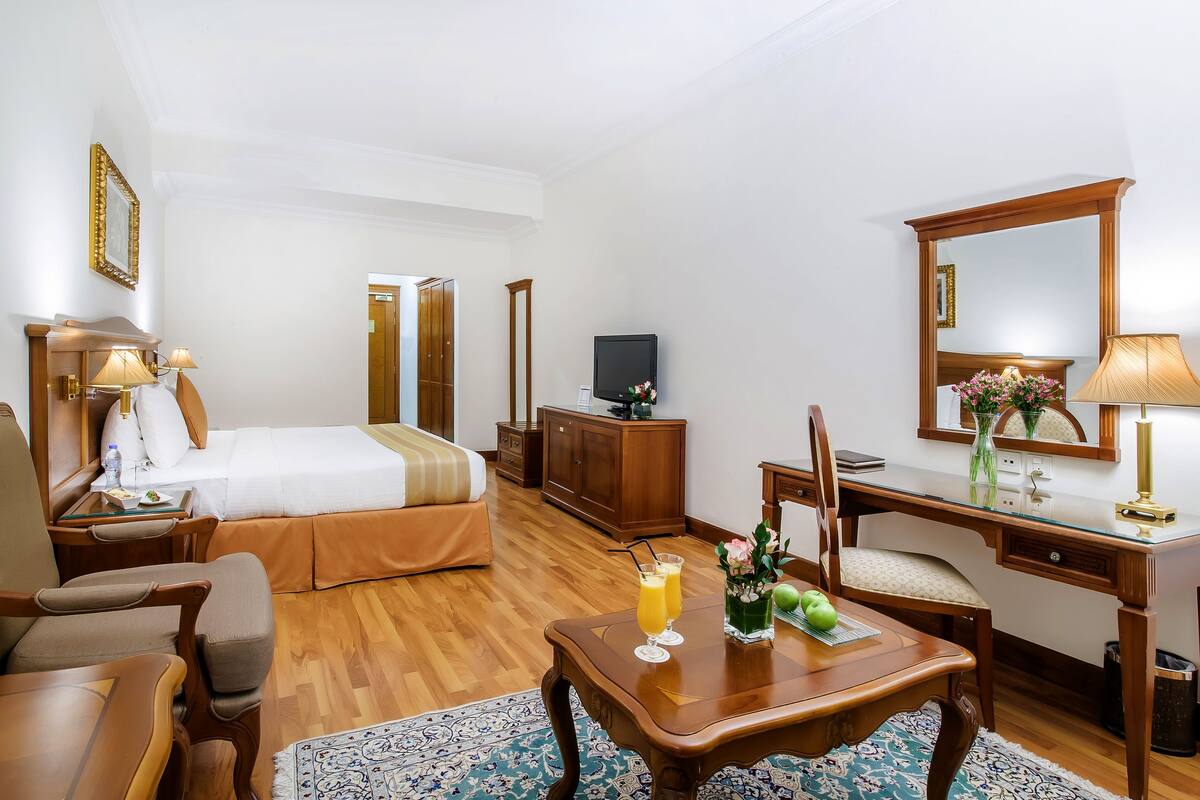 A hotel room with a bed, a desk, a chair, a TV, and a mirror.