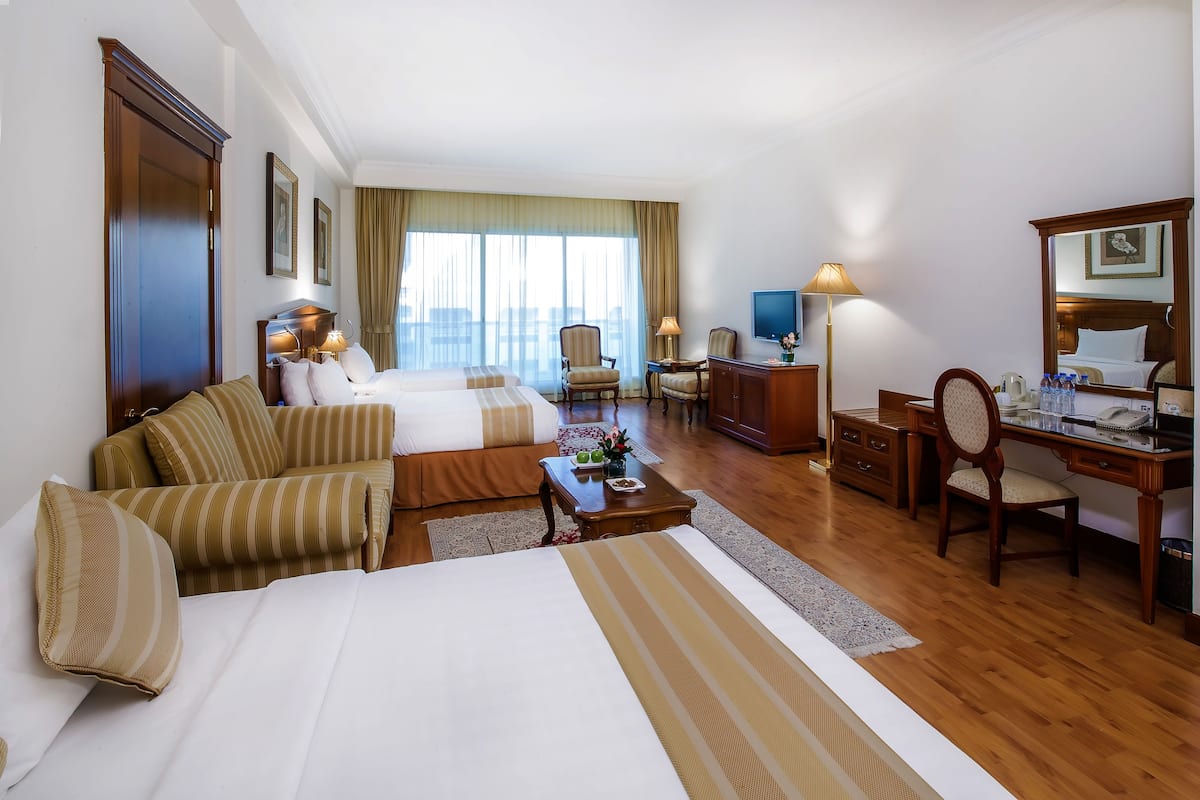 A hotel room with two beds, a desk, a chair, a TV, and a large window with curtains.
