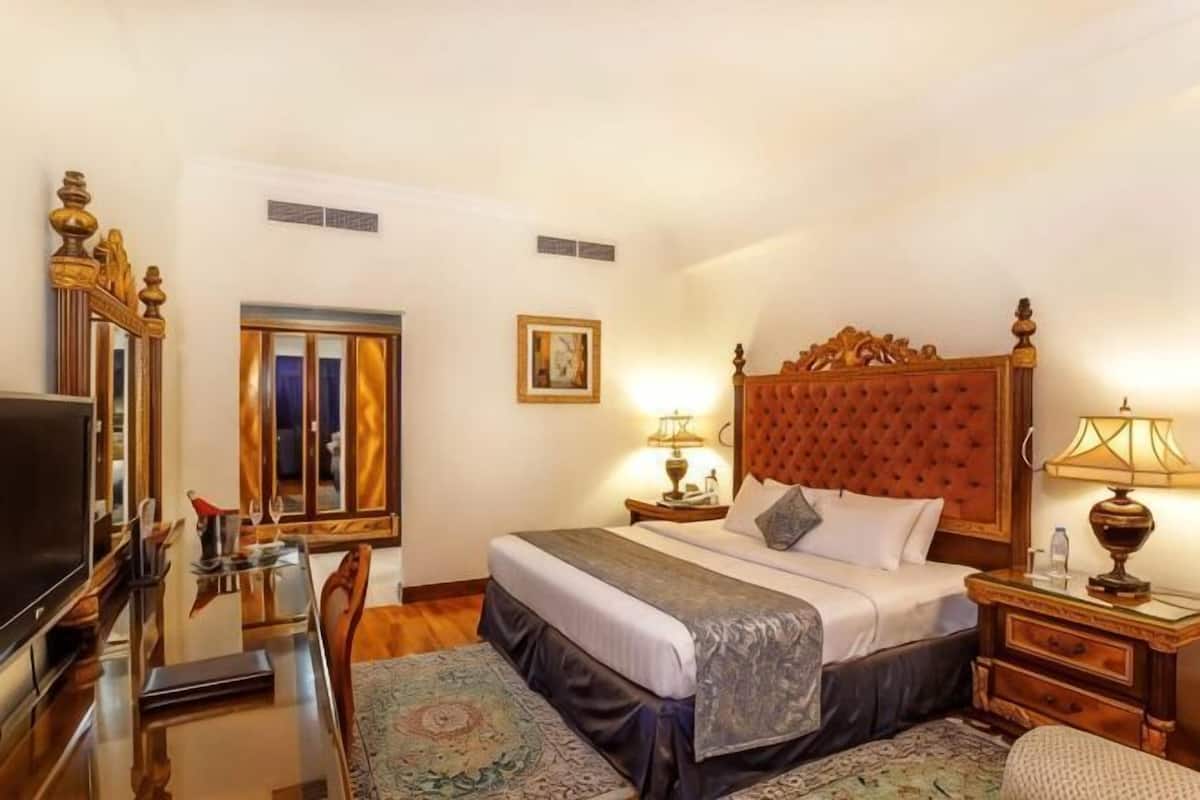 A hotel room with a bed, bedside tables, a TV, a desk, and a chair.