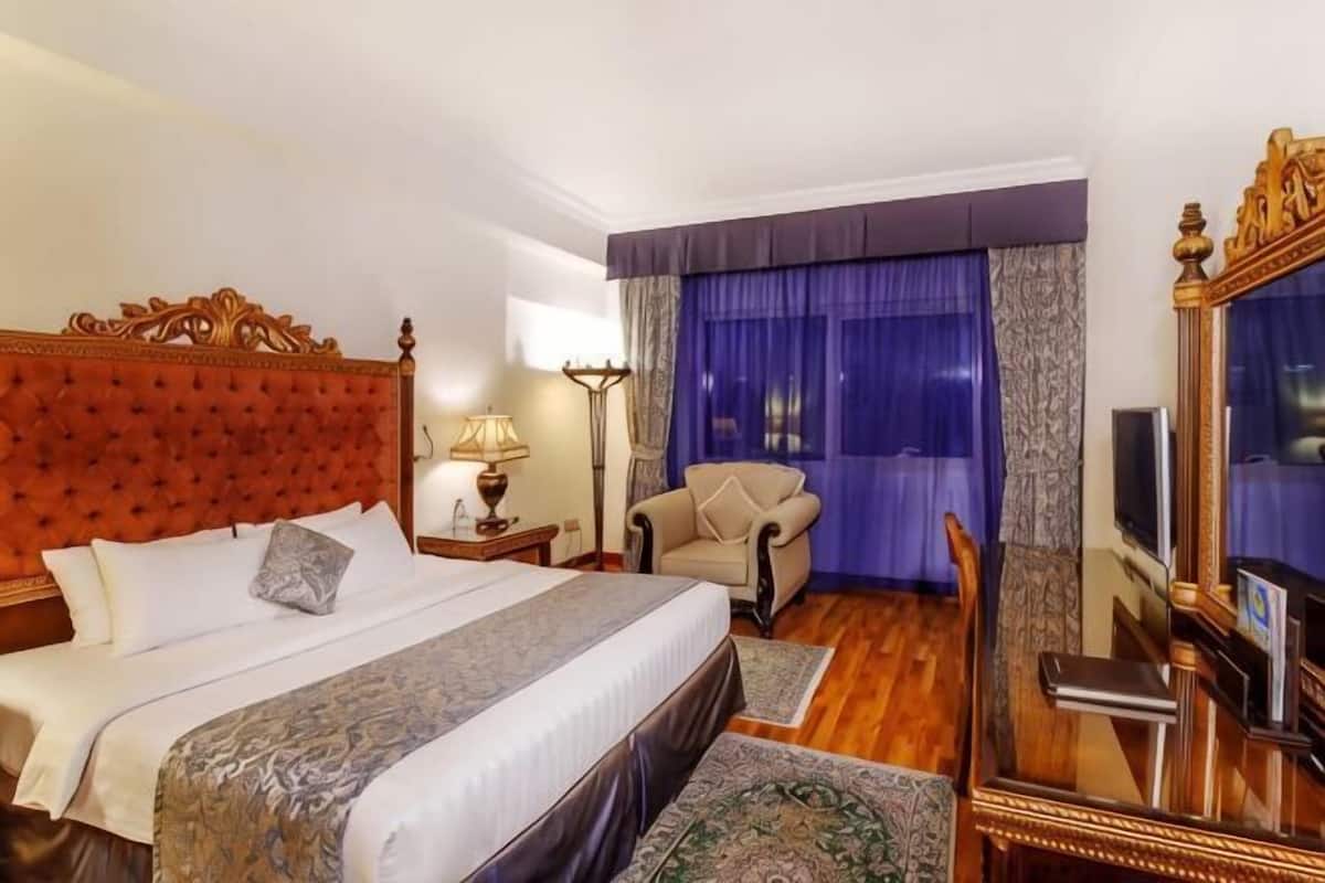 A hotel room with a large bed, a chair, a TV, and a mirror.